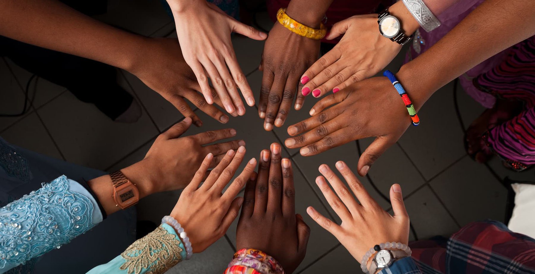 several hands, representing a diverse group of people, come together in a circle