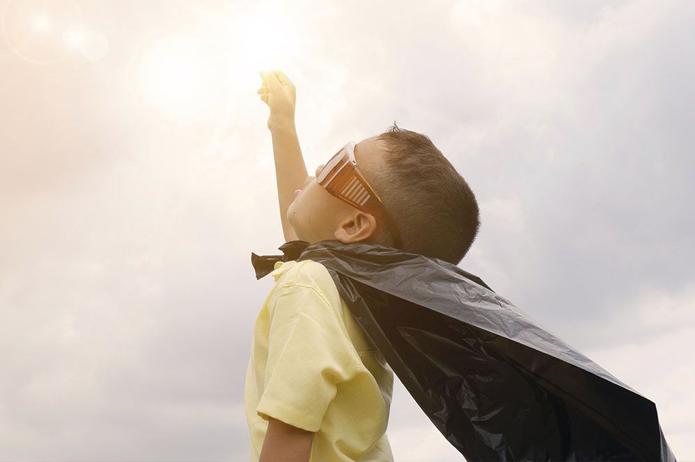 a little boy in glasses and cape looks up at a bright sky