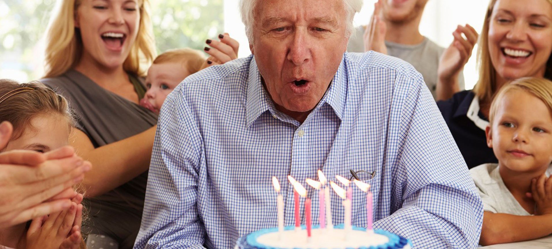 A man blows out the candles on his cake, surrounded by his family.