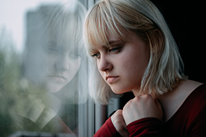 a sad, blonde woman stares out a window