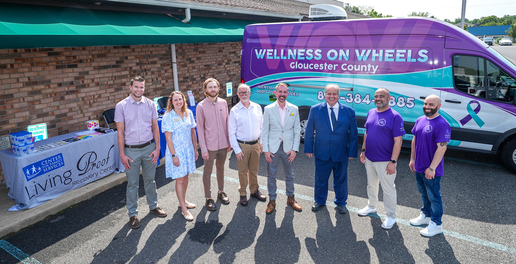 eight people stand in front of a van that is labelled WOW - Wellness on Wheels