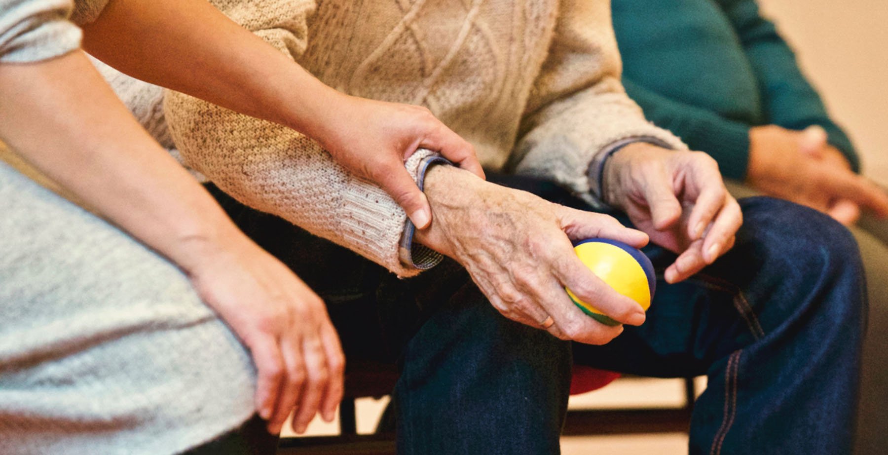 a person puts their hand on the arm of an older gentleman who is holding a ball in his hand