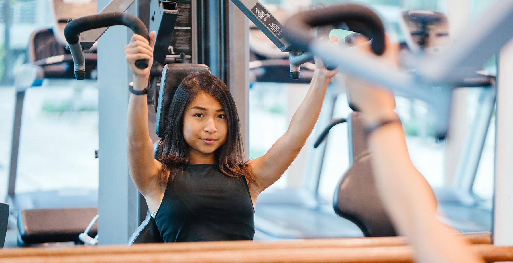 a woman raises her arms while on exercise equipment
