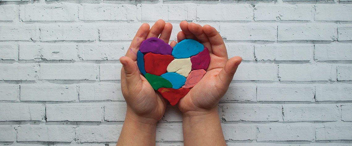 a multi-color clay heart being cradled in two hands